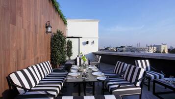 A rooftop terrace with a dining table set for six, surrounded by striped lounge chairs.