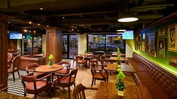 A restaurant interior with booths, tables, and chairs, featuring a checkered floor and a green accent wall with framed pictures.