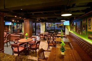 L’intérieur d’un restaurant, avec des banquettes, des tables et des chaises, présente un sol à carreaux et un mur d’accent vert orné de tableaux encadrés.