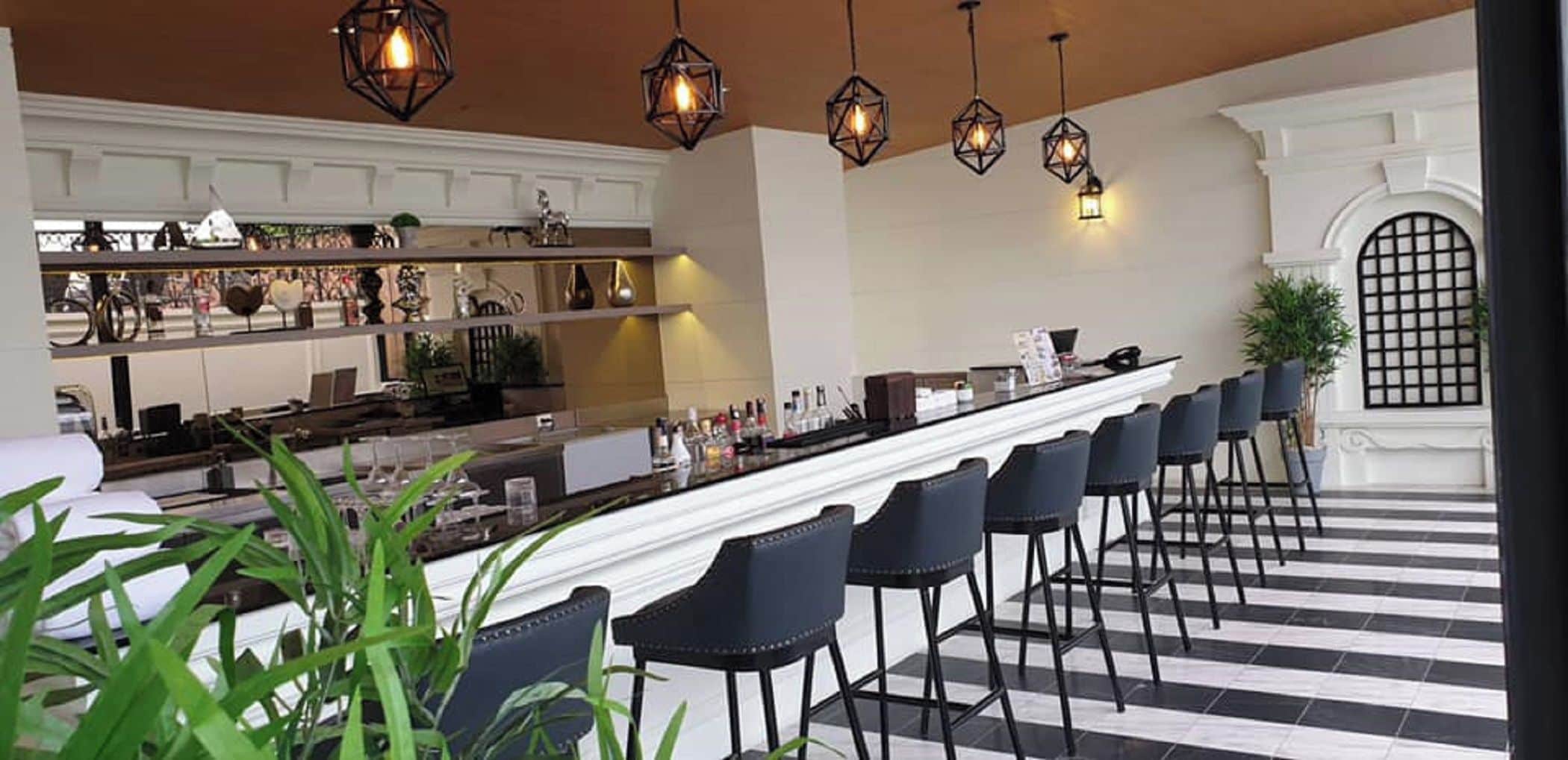Una zona de bar con una barra larga, varias sillas y lámparas geométricas colgantes.