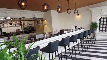 Una zona de bar con una barra larga, varias sillas y lámparas geométricas colgantes.