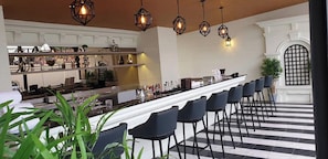 A bar area with a long counter, multiple chairs, and hanging geometric light fixtures.