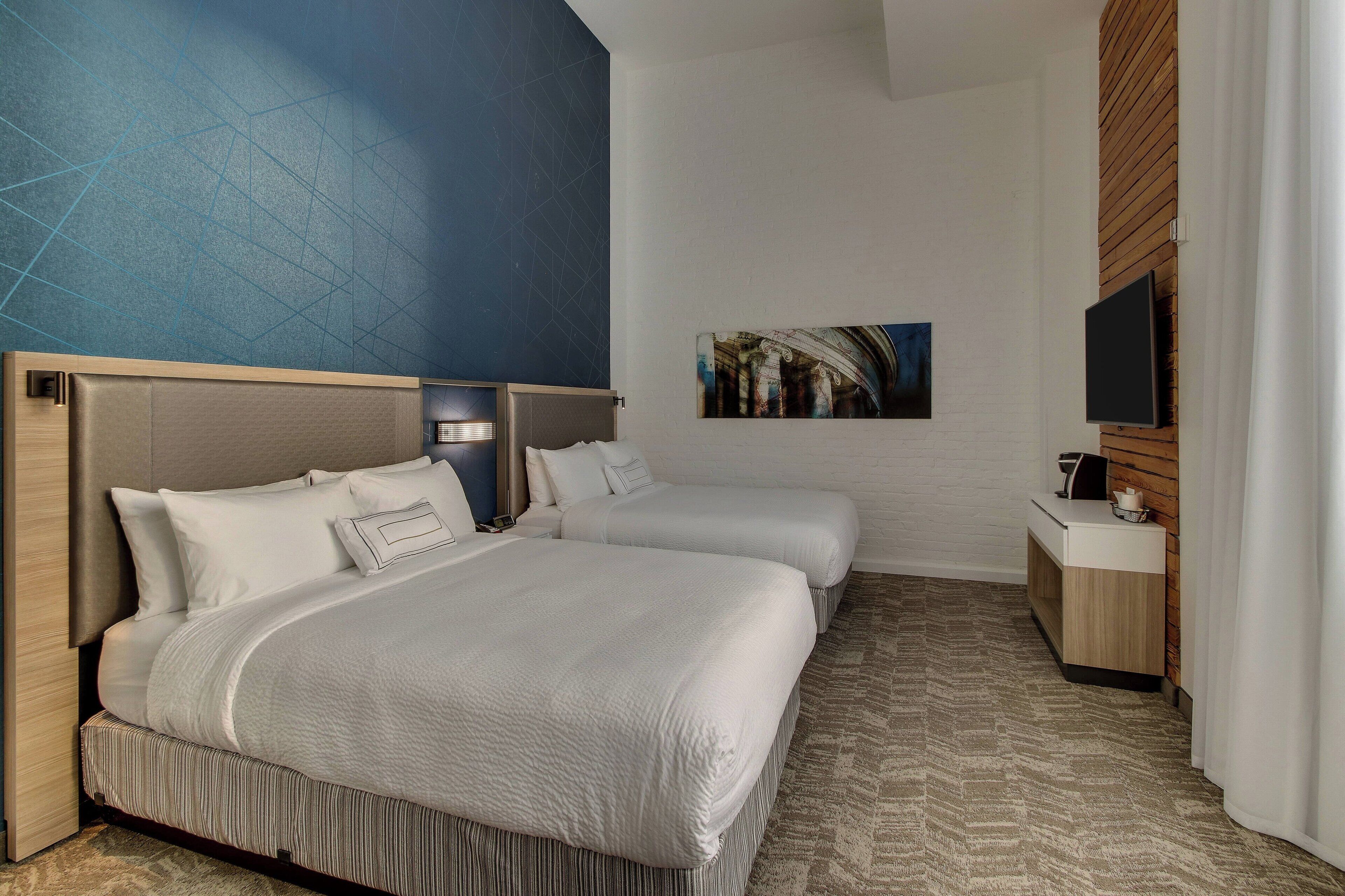 A hotel room with two beds, a flat-screen TV, a small bedside table, and a painting on the wall.