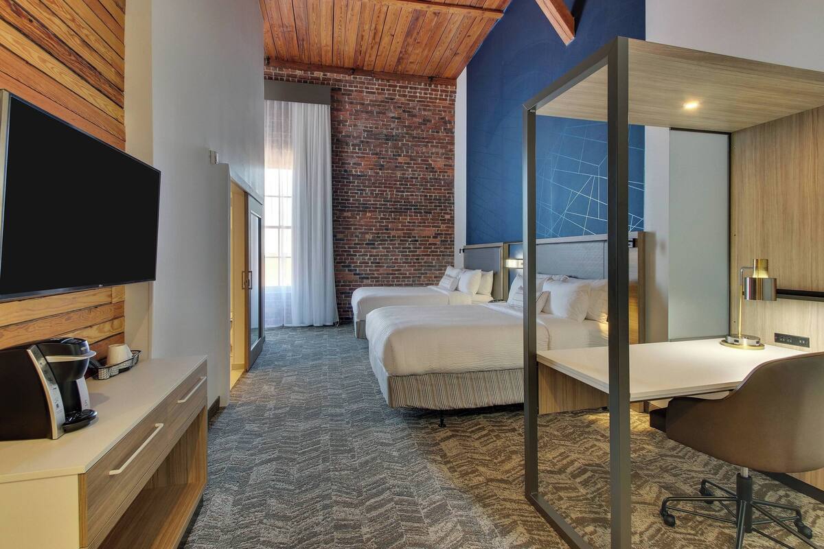 A hotel room with a large bed, a desk with a chair, a TV, and a coffee maker.