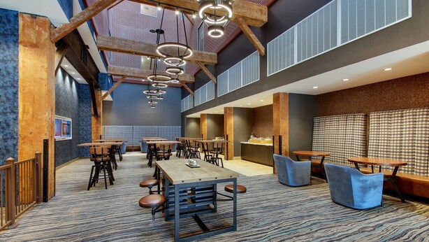 A spacious indoor area with multiple tables and chairs, a patterned carpet, and a high ceiling with exposed beams and circular light fixtures. - SpringHill Suites by Marriott Montgomery Downtown (Montgomery)
