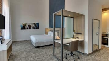 Habitación de hotel con cama, escritorio, silla, espejo y un cuadro en la pared.
