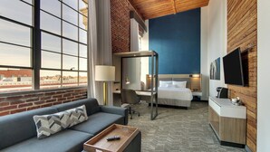 A hotel room with a large window, a sofa, a desk, a bed, and a TV mounted on the wall. - SpringHill Suites by Marriott Montgomery Downtown (Montgomery)
