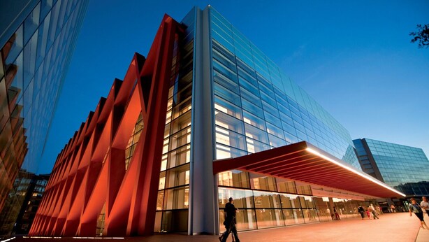 Un edificio moderno con fachada de vidrio y una estructura roja en primer plano.