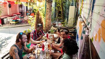 Un groupe de personnes est réuni autour d’une table en bois, à l’extérieur, et déguste divers plats et boissons.