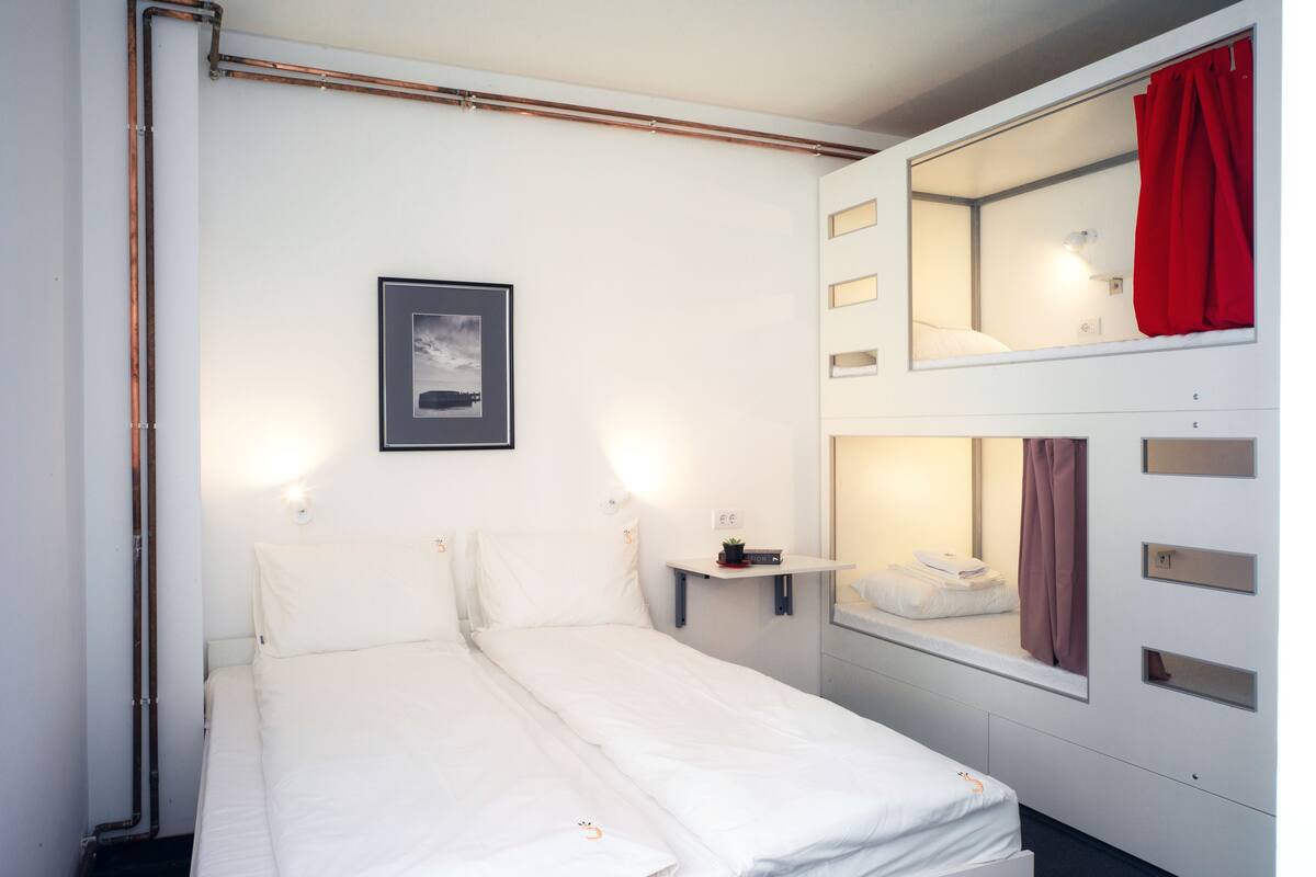 A bunk bed room with a single bed, a small shelf with a clock, and a framed picture on the wall.