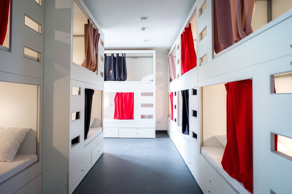 A corridor with bunk beds, each with a red curtain, and a central bed with a white mattress.