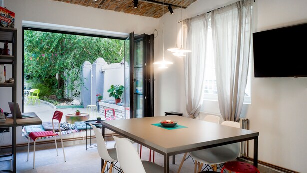 A modern dining area with a large table, chairs, and a television mounted on the wall. - Good People Design Hostel (Belgrade)