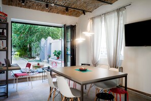 A modern dining area with a large table, chairs, and a television mounted on the wall. - Good People Design Hostel (Belgrade)