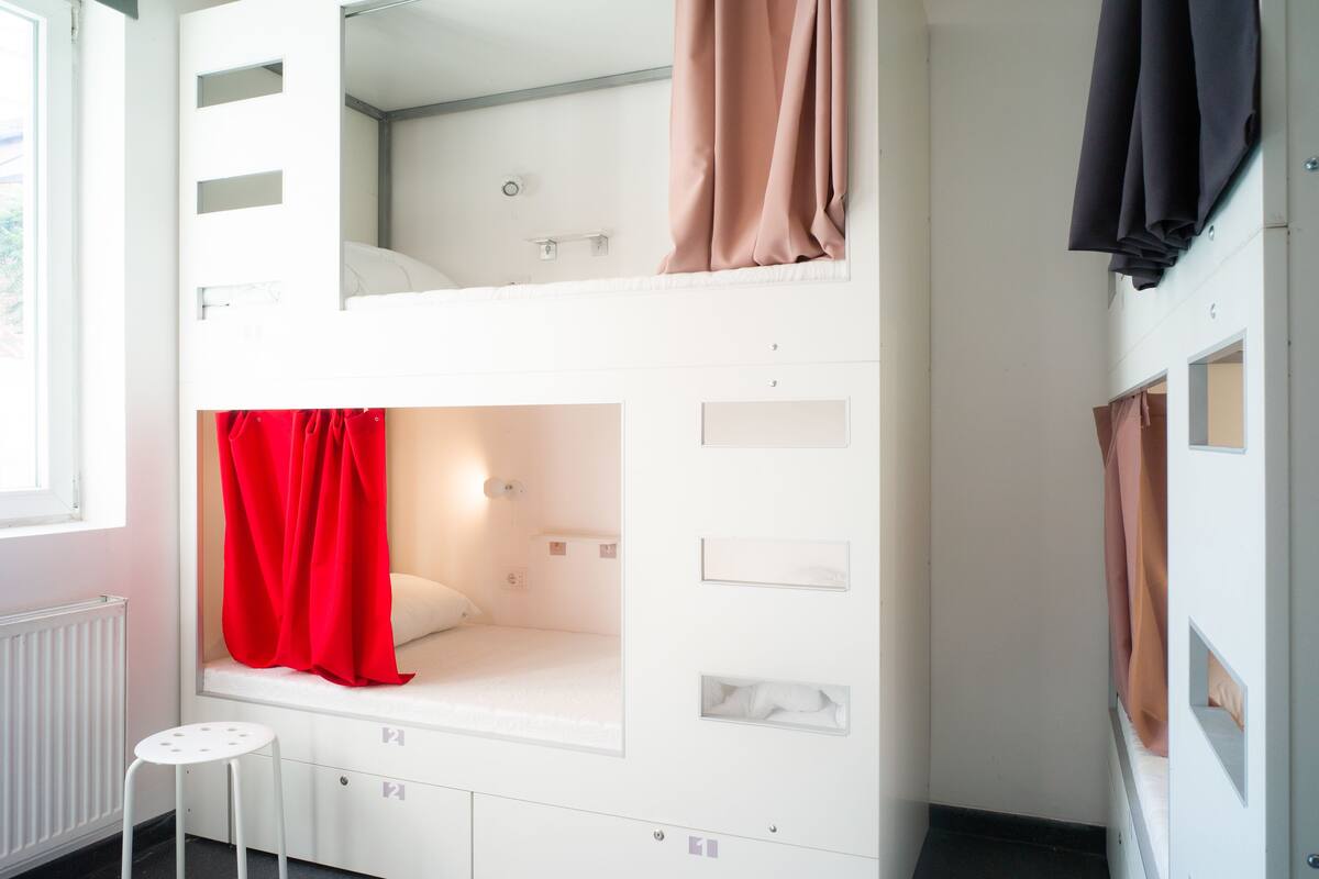 A bunk bed room with a window, a radiator, and a small stool.