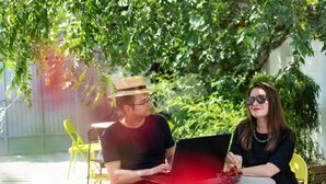 Two people sitting at an outdoor table with a laptop and a bowl of fruit. - Good People Design Hostel (Belgrade)