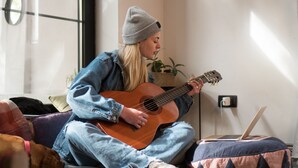 A person sitting on a couch playing a guitar, with a laptop on a bean bag beside them. - Good People Design Hostel (Belgrade)