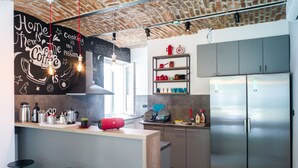 A modern kitchen with a brick ceiling, stainless steel appliances, and a bar area with stools. - Good People Design Hostel (Belgrade)