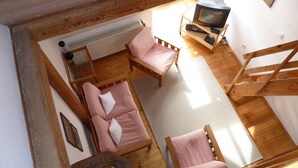 Een gezellige kamer met houten vloer, een bank, een fauteuil, een klein tafeltje, een radiator en een televisie op een standaard.