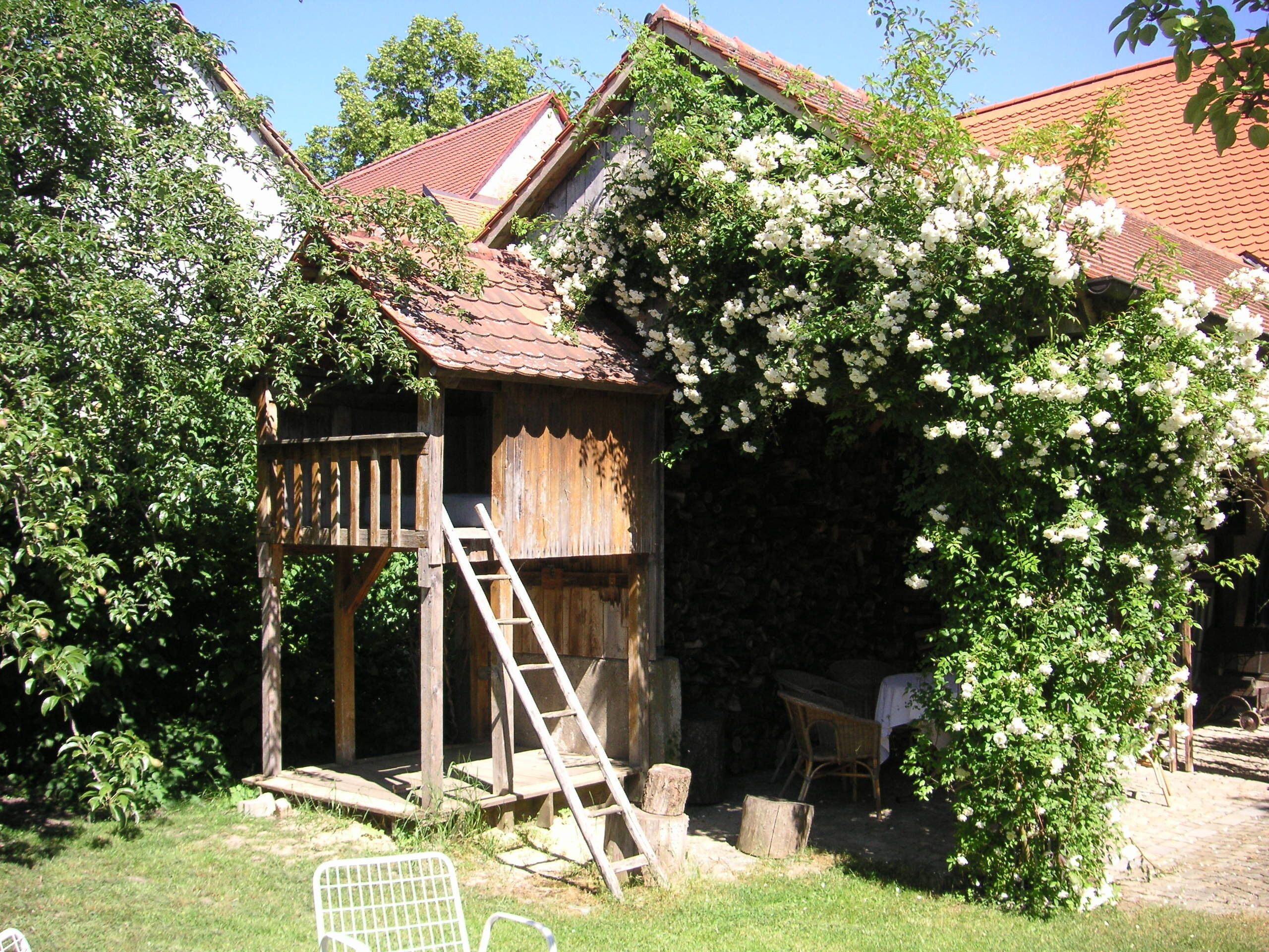En rustik träbyggnad med ett sluttande tak, en trätrappa som leder upp till en veranda och en vit stol utanför.