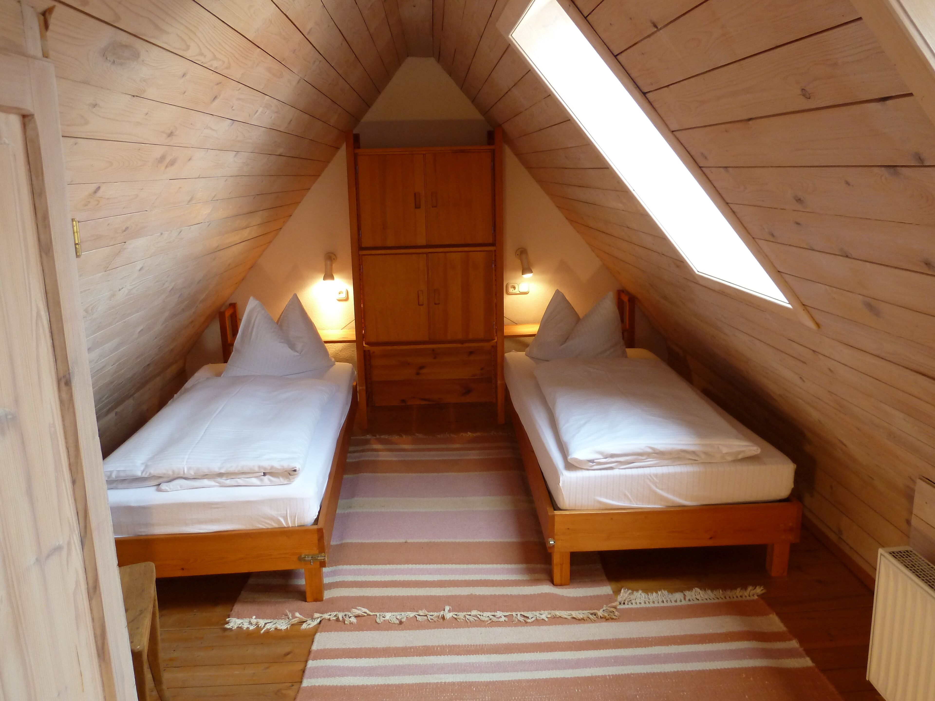 Una camera da letto mansardata con due letti singoli, un'armadietto in legno e un soffitto inclinato con finestra a lucernario.