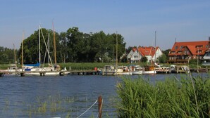 Ein Yachthafen mit vor Anker liegenden Booten, einer Mole und Gebäuden mit roten Dächern im Hintergrund.
