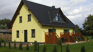 Ein zweistöckiges Haus mit einem geneigten Dach, einer Holztreppe und einem umzäunten Garten.