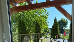 A window with a seagull on a stand, a wooden pergola, and a view of a garden with trees and a boat. - Holidays directly on the water with great additional services (Ziemitz)