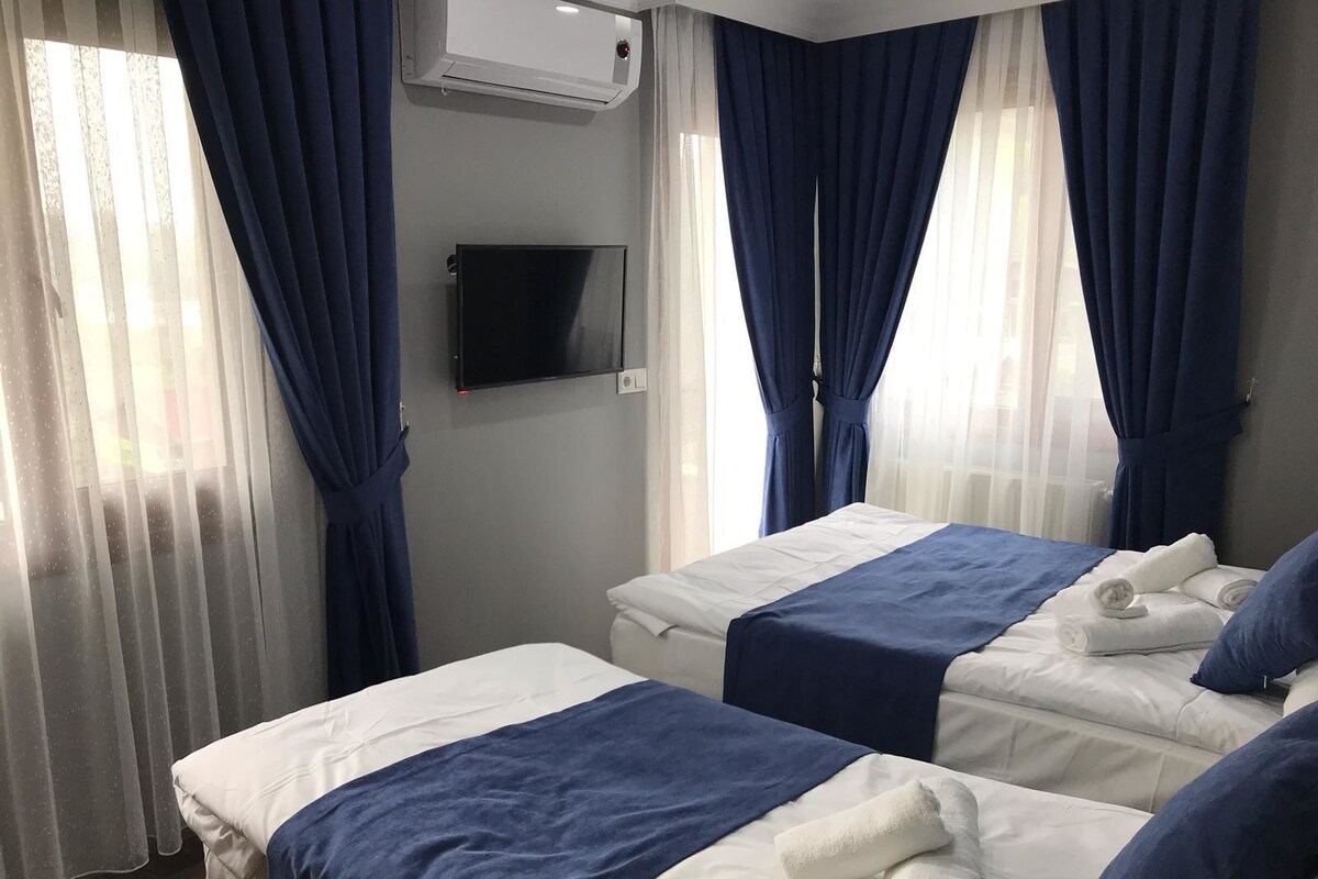 Habitación de hotel con dos camas, cada una con colcha azul y blanca, y un televisor de pantalla plana montado en la pared.
