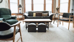 Un salon chaleureux avec un fauteuil vert, un canapé en cuir agrémenté de coussins à motifs, une table basse en bois et deux poufs noirs.