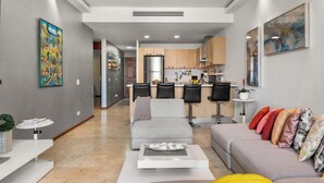 Een moderne woonkamer met een grijze bank, een salontafel, en een keuken op de achtergrond.