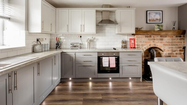 A modern kitchen with white cabinets, a built-in oven, and a brick fireplace. - Neds Brae House (Ballymena)