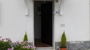 Une entrée d’immeuble blanche avec une porte noire, une plaque portant le numéro « 31 » et un petit panneau indiquant « Appartement ».