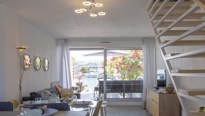 A modern living room with a dining area, large windows with a view of a marina, a staircase, and a minimalist design. - Holidays in MARINA in PORT CAMARGUE and 100m from the beach! (Le Grau-du-Roi)