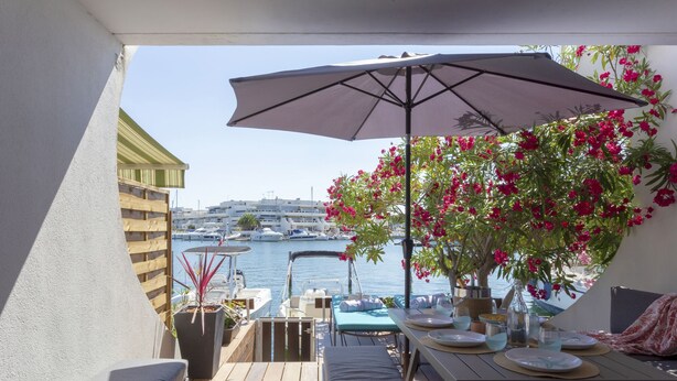 A wooden deck with outdoor furniture, a table set for dining, and a large umbrella providing shade. - Holidays in MARINA in PORT CAMARGUE and 100m from the beach! (Le Grau-du-Roi)