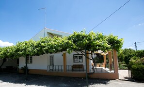 A two-story building with a white facade and a brown base. There is a covered porch with a bench and a small table.