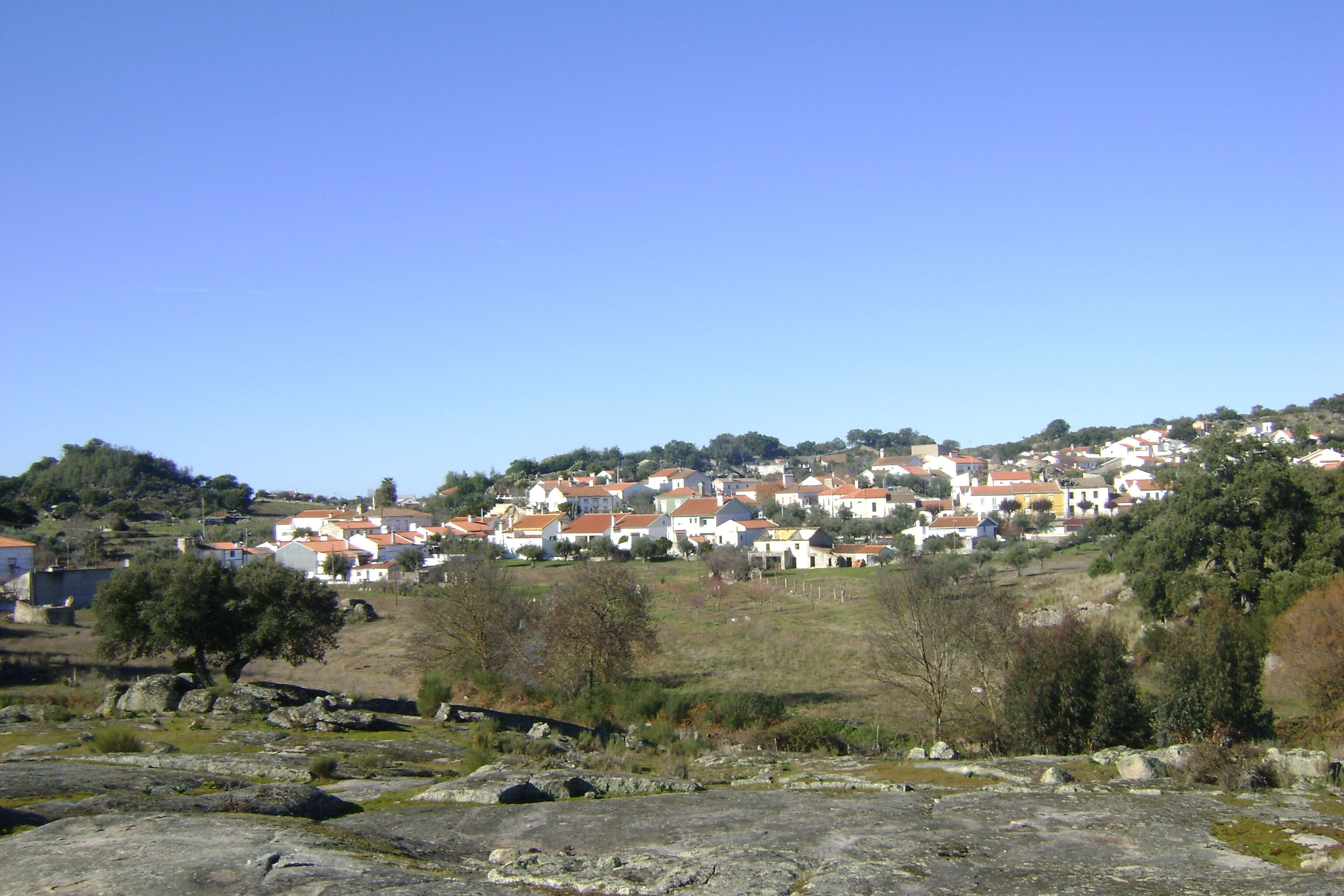 Ein Dorf an einem Hang mit traditionellen Häusern, einem felsigen Vordergrund und spärlicher Vegetation.