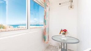 A small room with a window overlooking a beach, a table with a vase of flowers, and a flag on the wall. - 2 bedroom amazing apartment in Razanac (Razanac)