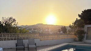 A swimming pool with a view of the sunset and a fence with chairs. - Traditional family villa, private pool and hillside views, 5 mins to Moraira. (Teulada)