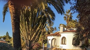 A stone-paved pathway leading to a white building with a tiled roof, surrounded by palm trees and other vegetation. - Traditional family villa, private pool and hillside views, 5 mins to Moraira. (Teulada)