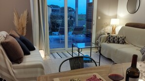 Una sala de estar con un sofá, una mesa de comedor con comida y bebida, y vistas al exterior a través de una puerta de vidrio.