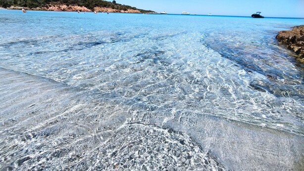 Una playa despejada con rocas visibles y un barco a lo lejos.