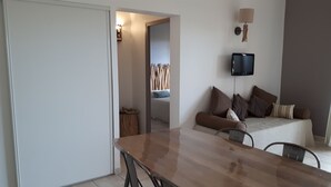 Una sala de estar moderna con una mesa de comedor de madera, un sofá con varios cojines, un televisor montado en la pared y una lámpara de pared decorativa.