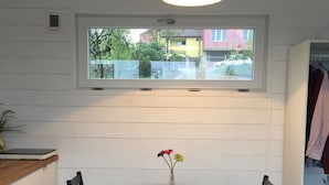 Un comedor con una mesa redonda, dos sillas, un florero con flores y una ventana sobre la mesa.
