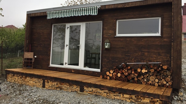 Una cabaña de madera con puerta de vidrio, una pequeña terraza y una pila de leña.