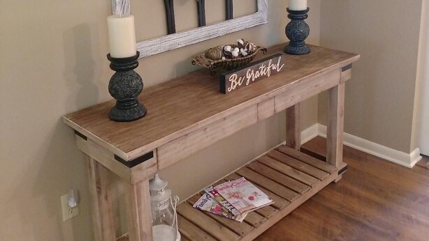Une console en bois agrémentée d’un miroir décoratif, de deux bougies, d’une plante en pot et d’une petite pancarte portant l’inscription « Soyez reconnaissant ».