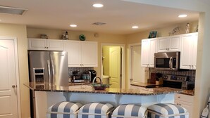 Una cocina moderna con gabinetes blancos, electrodomésticos de acero inoxidable y una isla central con taburetes a rayas.
