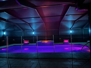 A modern, dimly lit indoor pool area with geometric ceiling design and purple lighting.