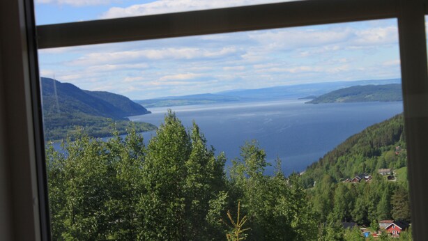 A view through a window of a lake surrounded by mountains and trees.
