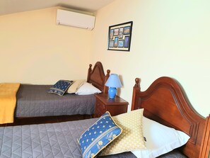 A hotel room with two beds, a nightstand with a lamp, a wall-mounted air conditioner, and a framed picture. - Casa Límia (Ponte de Lima)