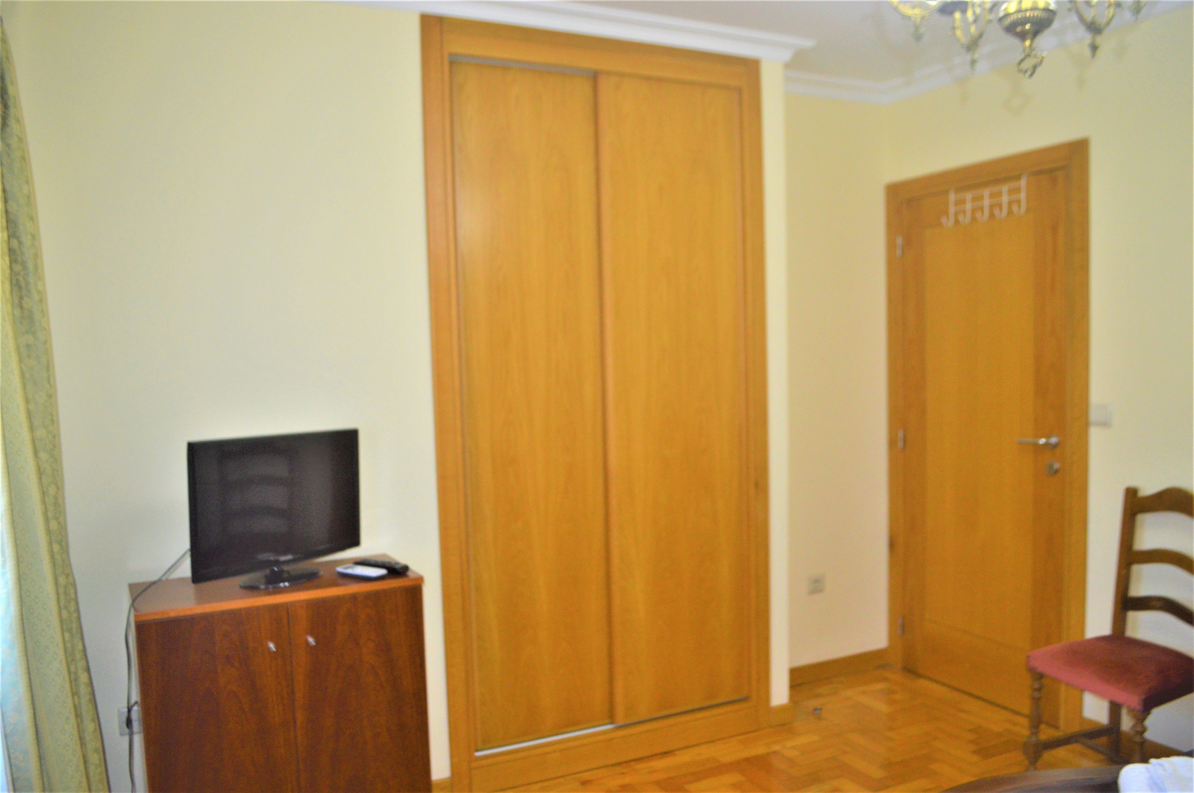 A room with a wooden wardrobe, a television on a wooden cabinet, and a red chair.